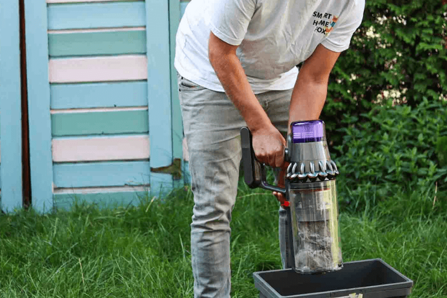 Der Inhalt des Staubbehälters von einem Akkusauger wird in der Mülltonne entsorgt
